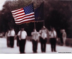 U.S. flag held high by people standing in a line during a parade; background is hazy and out of focus.